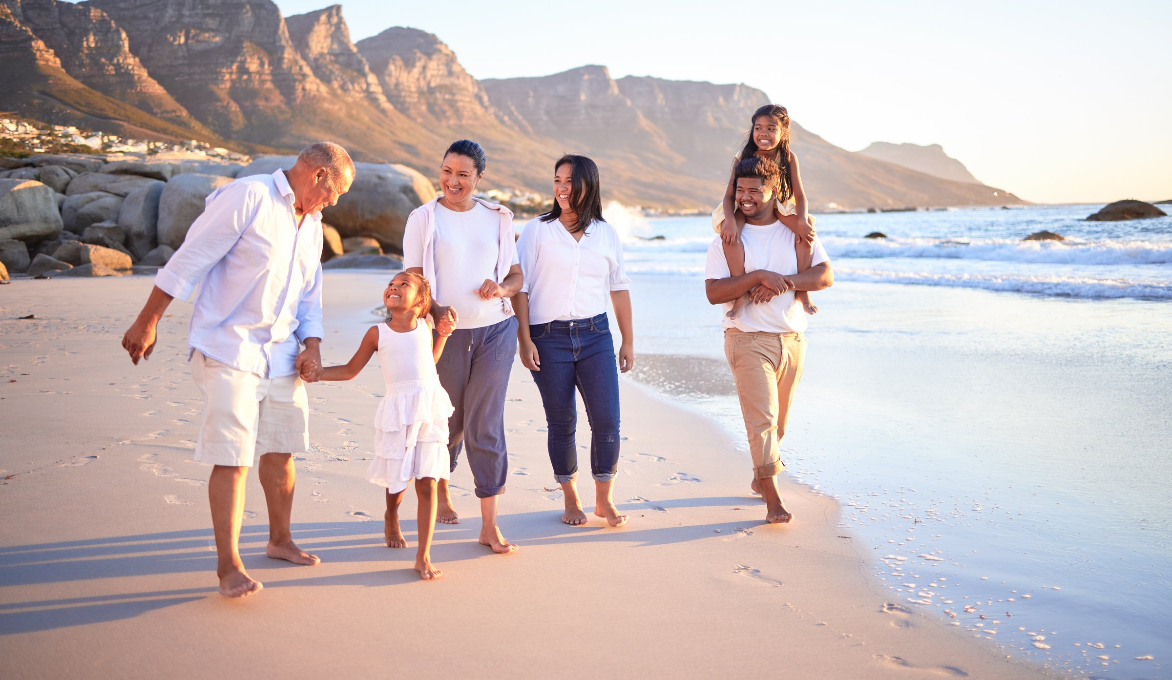 Familia de tres generaciones caminando por la playa con monta&ntilde;as al fondo
